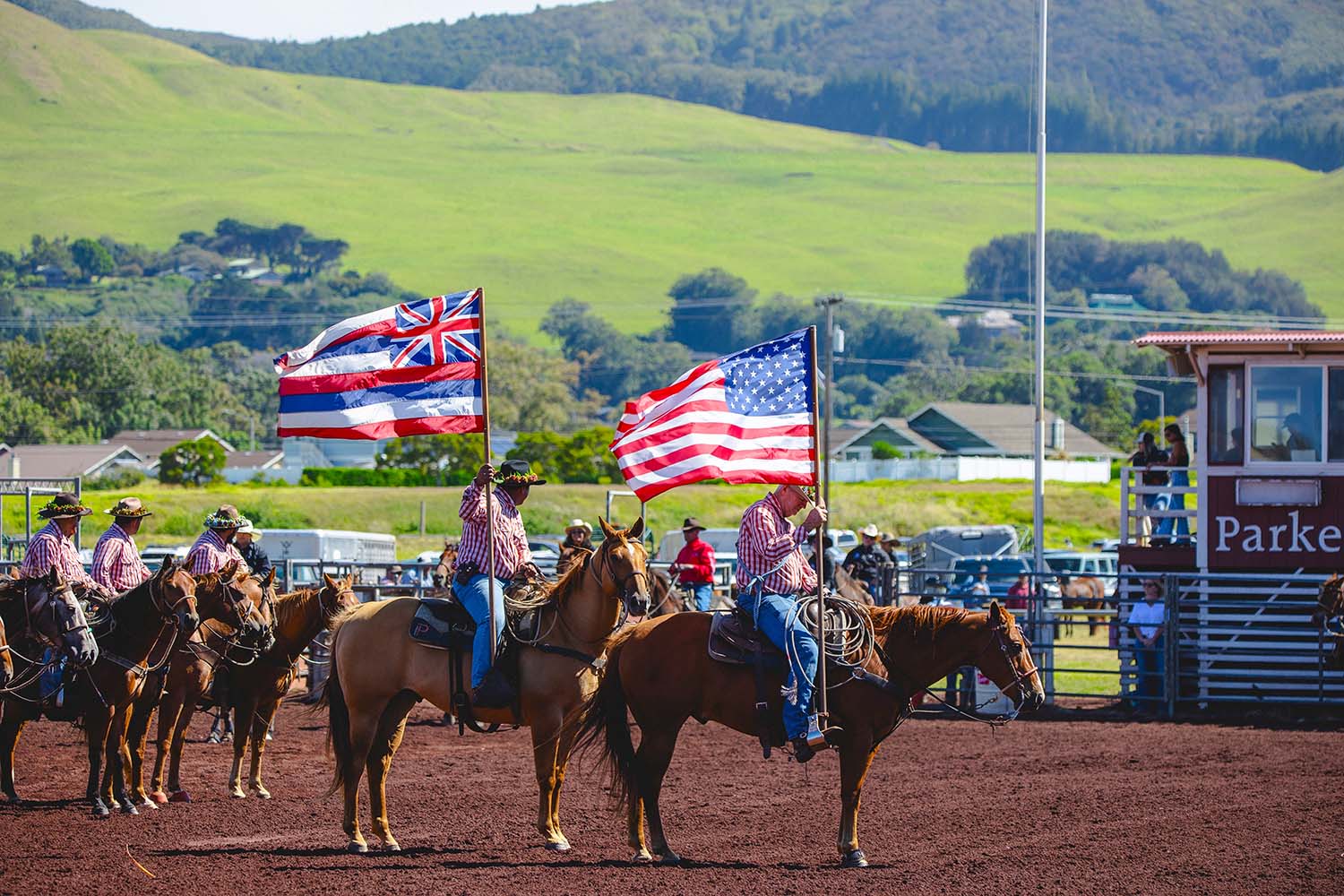 Two paniolo on horseback carrying the Hawaiian and American flags during the grand entry of the annual July 4th Rodeo.