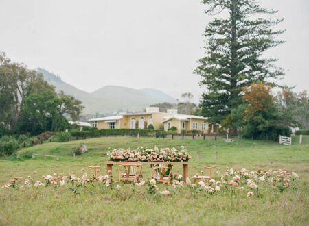 Reception table decorated with florals in the middle of a field in front of a historic home at Parker Ranch
