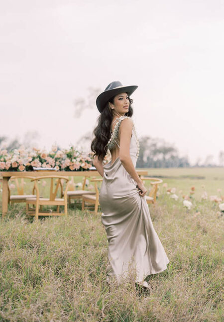 Bride wearing a cowboy hat standing in a field in front of a reception table decorated with florals