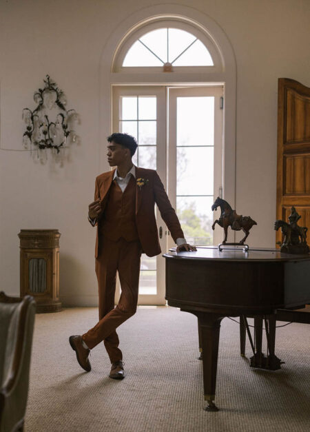 Groom standing next to a piano inside a historic home at Parker Ranch